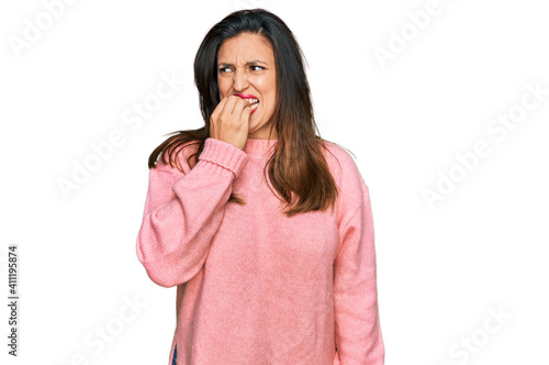 Beautiful hispanic woman wearing casual winter sweater looking stressed and nervous with hands on mouth biting nails. anxiety problem.