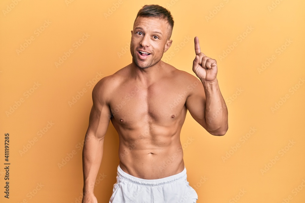 Fototapeta premium Handsome muscle man standing shirtless pointing finger up with successful idea. exited and happy. number one.