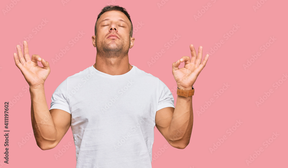 Handsome muscle man wearing casual white tshirt relaxed and smiling with eyes closed doing meditation gesture with fingers. yoga concept. Handsome muscle man wearing casual white tshirt relaxed and smiling with eyes closed doing meditation gesture with fingers. yoga concept.