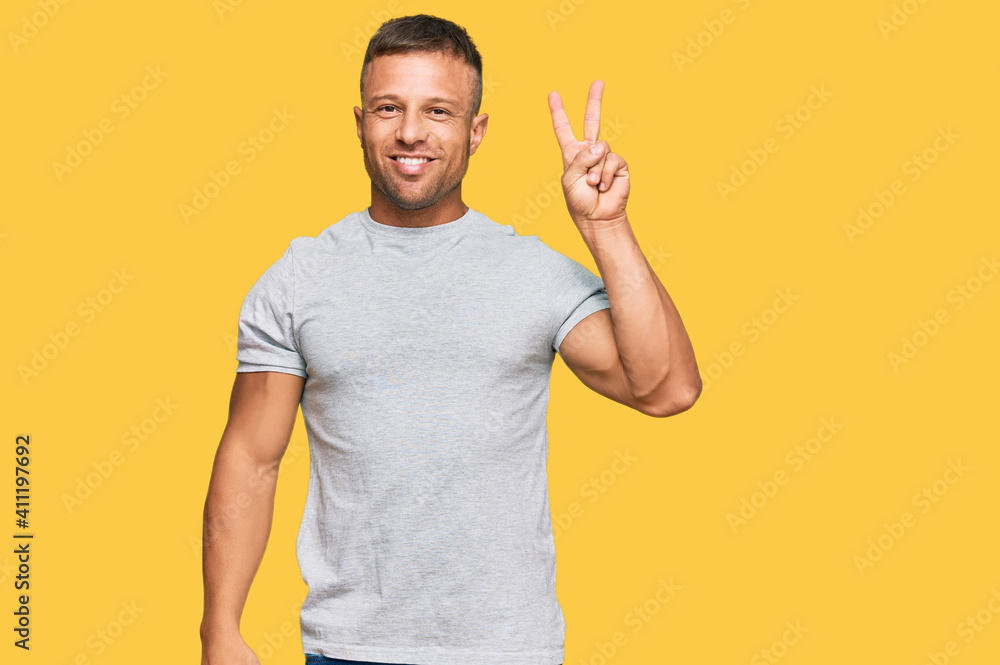 Handsome muscle man wearing casual grey tshirt smiling with happy face winking at the camera doing victory sign. number two. Handsome muscle man wearing casual grey tshirt smiling with happy face winking at the camera doing victory sign. number two.