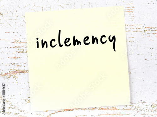 Yellow sticky note on wooden wall with handwritten word inclemency