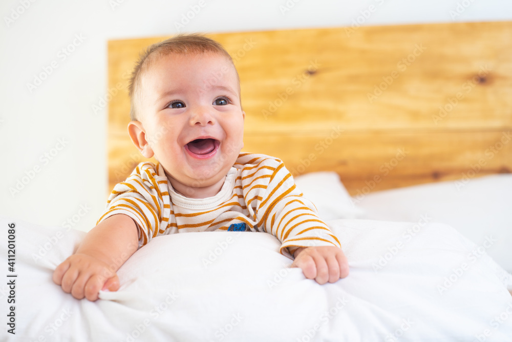 in a room a beautiful and funny happy smiling baby plays with his colorful toys and teddy bear on a wooden bed with beige blankets of white sheets in a room a beautiful and funny happy smiling baby plays with his colorful toys and teddy bear on a wooden bed with beige blankets of white sheets
