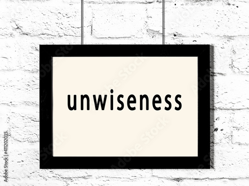 Black frame hanging on white brick wall with inscription unwiseness photo