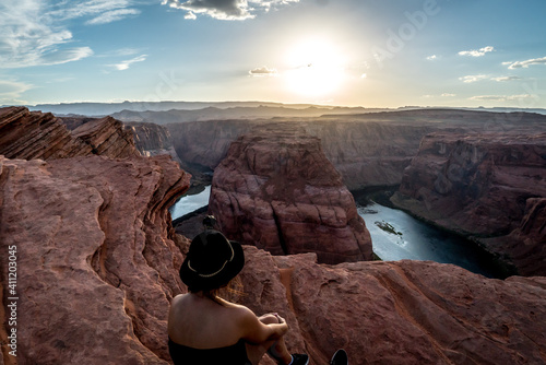 Eine junge Frau sitzt am Rande einer Klippe und schaut dem Sonnenuntergang zu. Horseshoe Bend - Utah - USA.