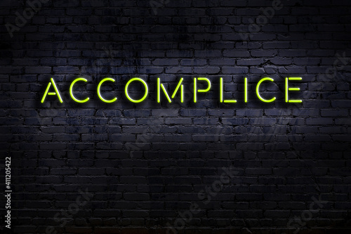 Neon sign. Word accomplice against brick wall. Night view