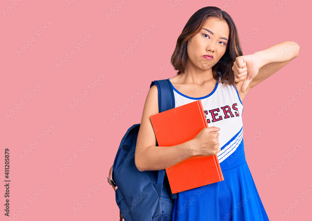 Young beautiful chinese girl wearing cheerleader uniform and student backpack holding binder with angry face, negative sign showing dislike with thumbs down, rejection concept Young beautiful chinese girl wearing cheerleader uniform and student backpack holding binder with angry face, negative sign showing dislike with thumbs down, rejection concept