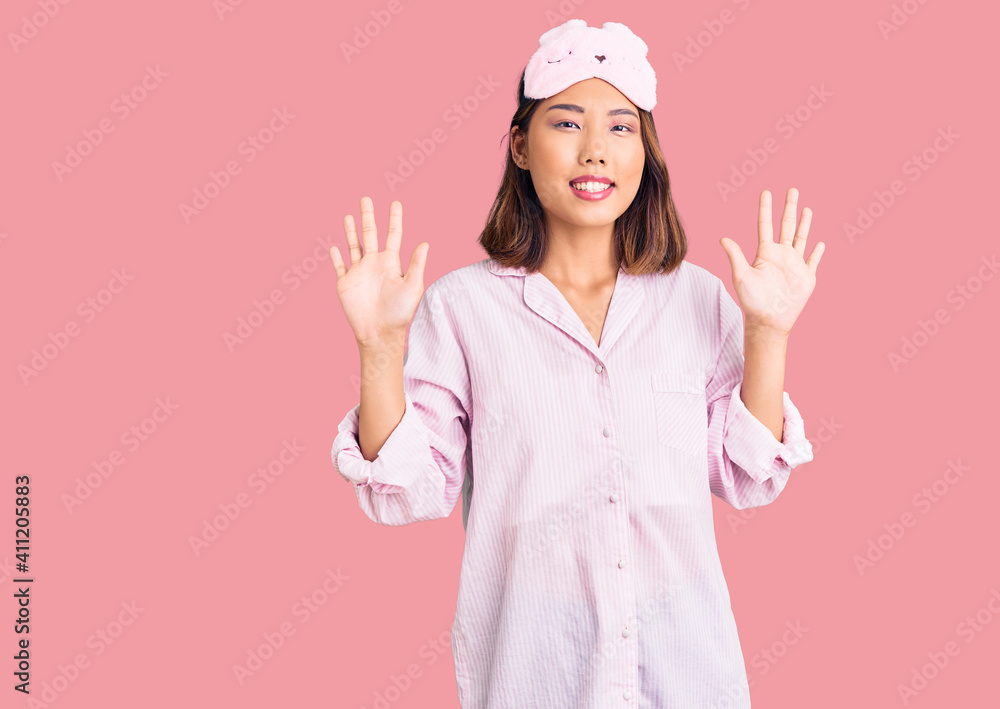 Young beautiful chinese girl wearing sleep mask and pajama showing and pointing up with fingers number ten while smiling confident and happy. Young beautiful chinese girl wearing sleep mask and pajama showing and pointing up with fingers number ten while smiling confident and happy.