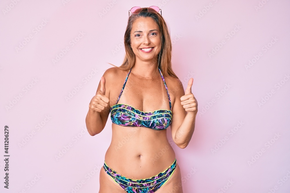 Naklejka premium Middle age hispanic woman wearing bikini success sign doing positive gesture with hand, thumbs up smiling and happy. cheerful expression and winner gesture.