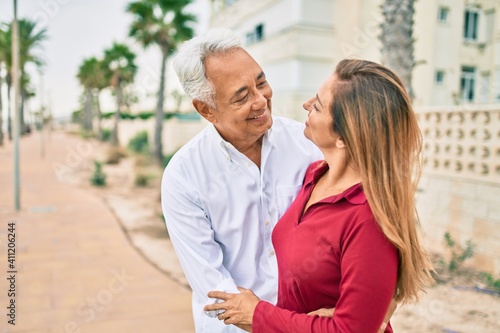 Middle age hispanic couple smiling happy and hugging walking at street.