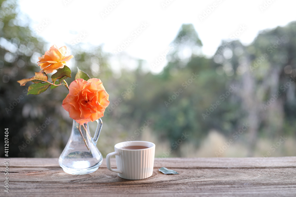 White tea cup and roses vase on wooden table
