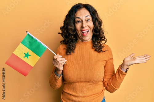 Middle age hispanic woman holding senegal flag celebrating achievement with happy smile and winner expression with raised hand