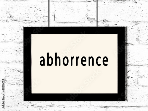 Black frame hanging on white brick wall with inscription abhorrence