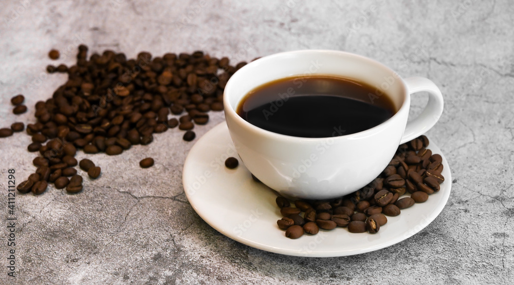 Side view of a cup of coffee surrounded with coffee beans against concrete background. Side view of a cup of coffee surrounded with coffee beans against concrete background.