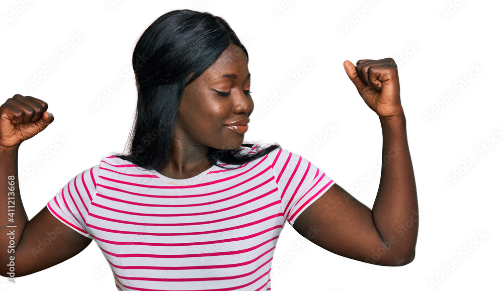 African young woman wearing casual striped t shirt showing arms muscles smiling proud. fitness concept. African young woman wearing casual striped t shirt showing arms muscles smiling proud. fitness concept.