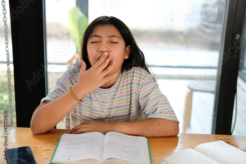 girl student yawning while reading book feeling tired bored sleepy. children education