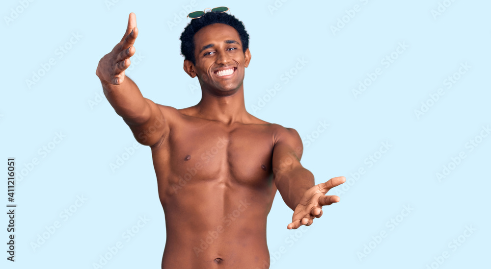 African handsome man wearing swimsuit and sunglasses looking at the camera smiling with open arms for hug. cheerful expression embracing happiness. African handsome man wearing swimsuit and sunglasses looking at the camera smiling with open arms for hug. cheerful expression embracing happiness.