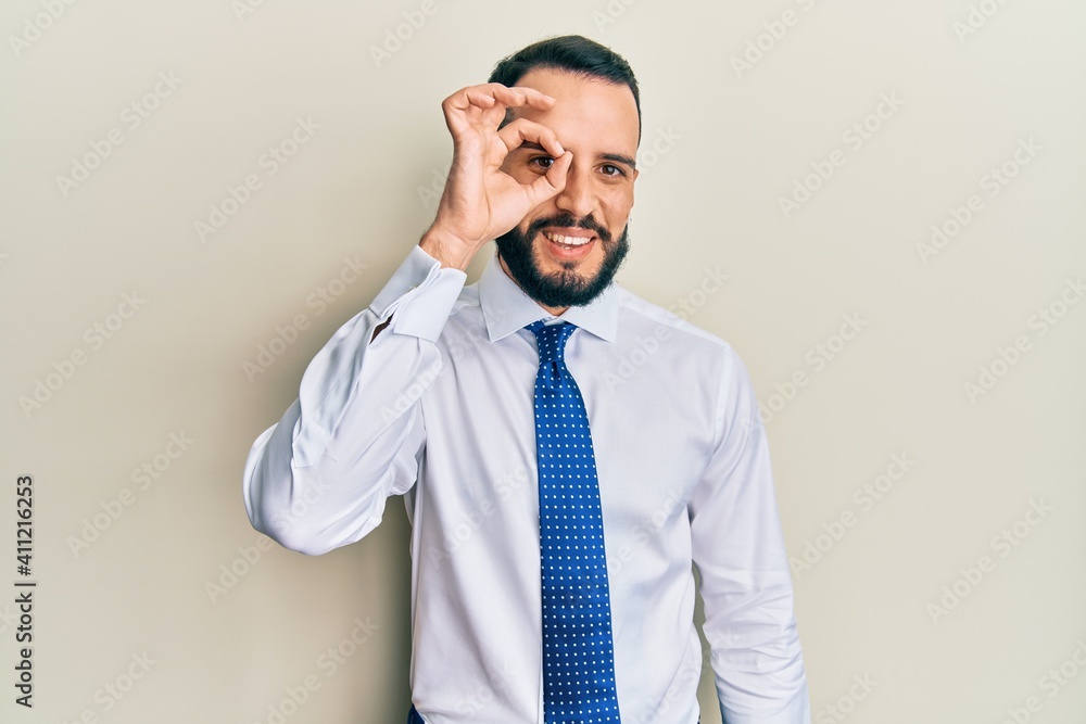 Young man with beard wearing business tie doing ok gesture with hand smiling, eye looking through fingers with happy face. Young man with beard wearing business tie doing ok gesture with hand smiling, eye looking through fingers with happy face.