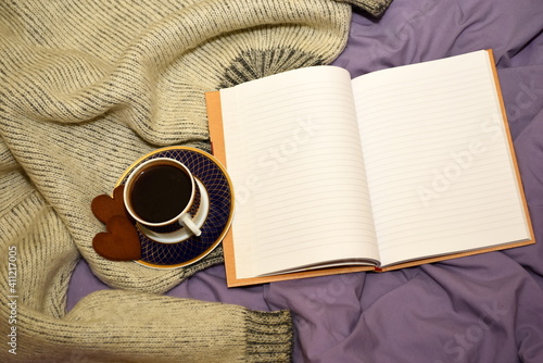 A cup of coffee  two gingerbread hearts and a blank open notebook on the bed. selective focus  copy space  softblurr effect