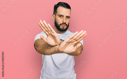 Young man with beard wearing casual white t shirt rejection expression crossing arms and palms doing negative sign, angry face