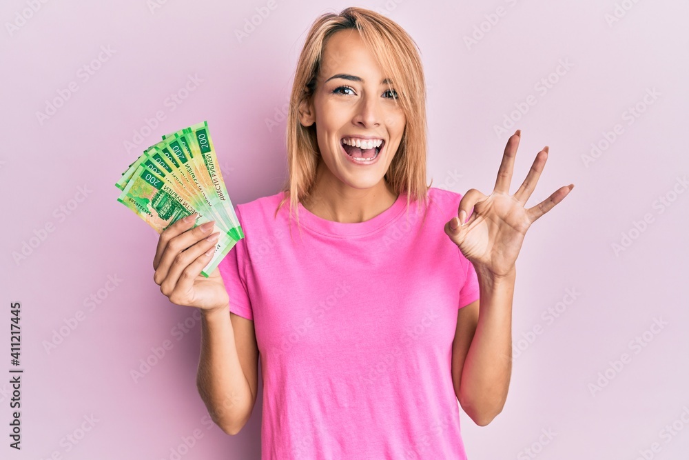 Beautiful blonde woman holding 200 russian ruble banknotes doing ok sign with fingers, smiling friendly gesturing excellent symbol Beautiful blonde woman holding 200 russian ruble banknotes doing ok sign with fingers, smiling friendly gesturing excellent symbol