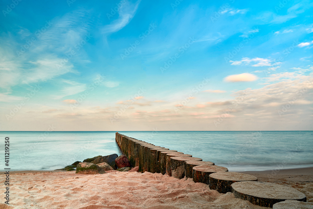 Sandy beach by the sea, wooden breakwater goes into the blue sky horizon