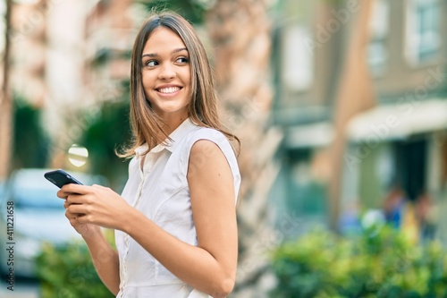 Beautiful latin teenager girl smiling happy using smartphone at the city.