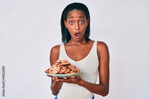 Young african american woman holding plate with cookies scared and amazed with open mouth for surprise  disbelief face