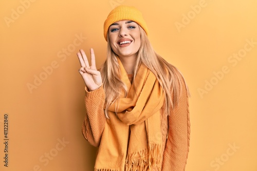 Young caucasian woman wearing wool winter sweater and cap showing and pointing up with fingers number three while smiling confident and happy. © Krakenimages.com