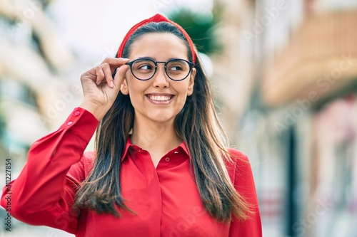 Young hispanic woman smiling happy touching his glasses at the city.