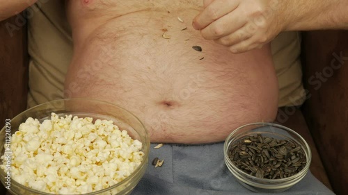 A Man With A Bare Belly Eating Sunflower Seeds