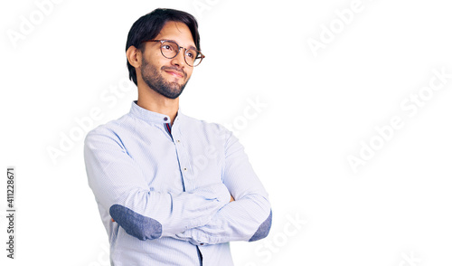 Handsome hispanic man wearing business shirt and glasses looking to the side with arms crossed convinced and confident