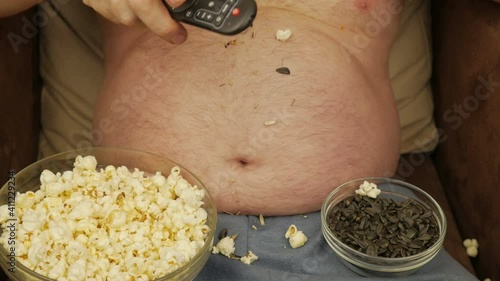A Man With A Bare Belly Drinks Beer And Eats Chips