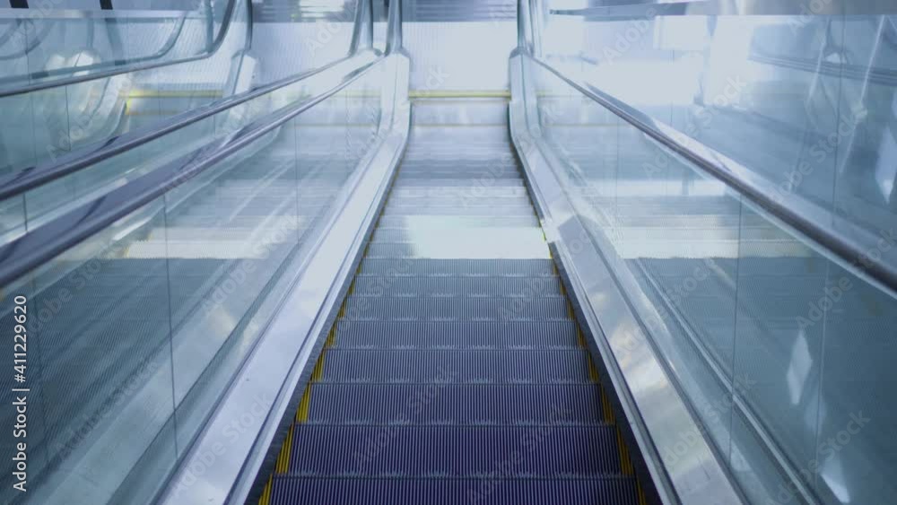 Escalator in a modern building. The escalator goes down. The camera moves with the escalator. Escalator in a modern building. The escalator goes down. The camera moves with the escalator.