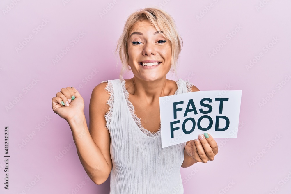 Young blonde girl eating fast food pizza and burger screaming proud, celebrating victory and success very excited with raised arm Young blonde girl eating fast food pizza and burger screaming proud, celebrating victory and success very excited with raised arm