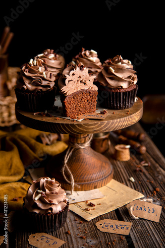 homemade tasty chocolate cupcakes with chocolate cream on wooden cake stand on rustic table. selective focus