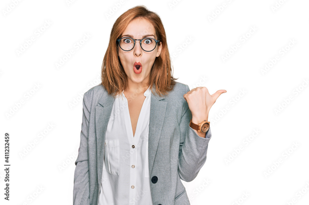Young caucasian woman wearing business style and glasses surprised pointing with hand finger to the side, open mouth amazed expression. Young caucasian woman wearing business style and glasses surprised pointing with hand finger to the side, open mouth amazed expression.