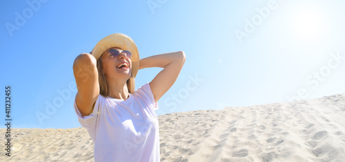 Young woman in a white T-shirt and hat on a background of sand and sky. The sun is shining