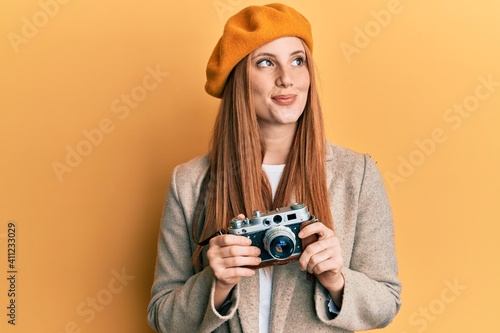 Young irish woman holding vintage camera smiling looking to the side and staring away thinking.