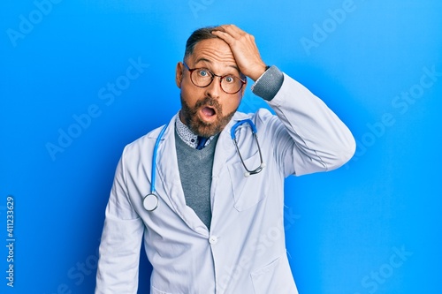 Handsome middle age man wearing doctor uniform and stethoscope surprised with hand on head for mistake, remember error. forgot, bad memory concept. © Krakenimages.com
