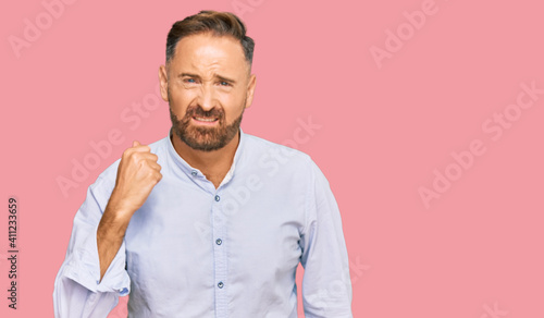 Handsome middle age man wearing business shirt angry and mad raising fist frustrated and furious while shouting with anger. rage and aggressive concept.