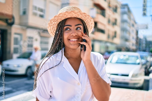 Young african american woman with braids smiling happy spaking on the phone outdoors on a sunny day of summer photo