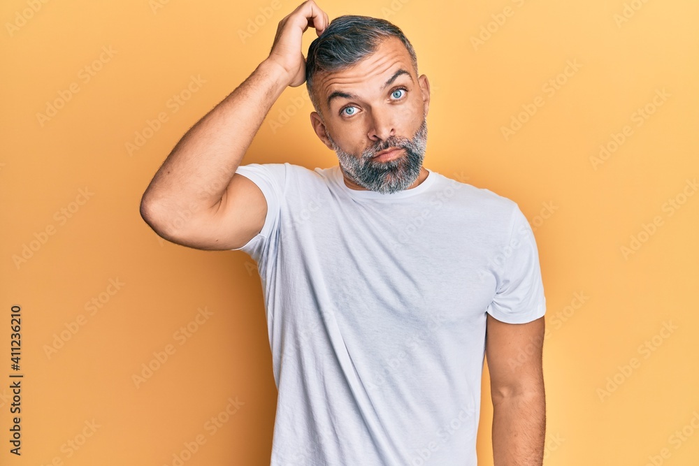 Middle age handsome man wearing casual white tshirt confuse and wonder about question. uncertain with doubt, thinking with hand on head. pensive concept. Middle age handsome man wearing casual white tshirt confuse and wonder about question. uncertain with doubt, thinking with hand on head. pensive concept.