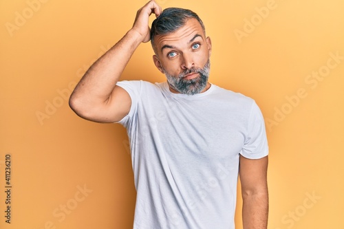 Middle age handsome man wearing casual white tshirt confuse and wonder about question. uncertain with doubt, thinking with hand on head. pensive concept. © Krakenimages.com