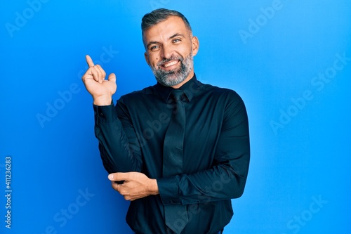 Middle age handsome man wearing business shirt and tie with a big smile on face, pointing with hand and finger to the side looking at the camera.