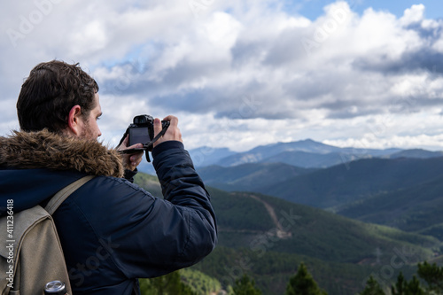 Photo of a attractive and young photographer in the middle of the wild looking through his camera zoom lens. Wearing winter clothes. Explorer, looking for animals