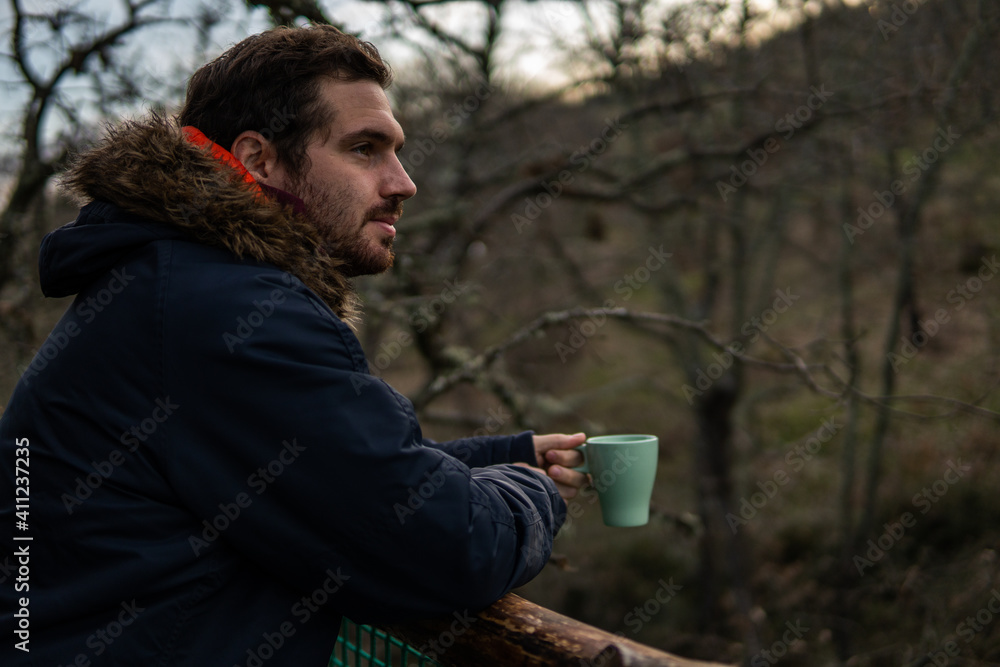 Photo of a young and attractive man having a coffee in the middle of a forest wearing winter clothes. Calm, empty place. Photo of a young and attractive man having a coffee in the middle of a forest wearing winter clothes. Calm, empty place.