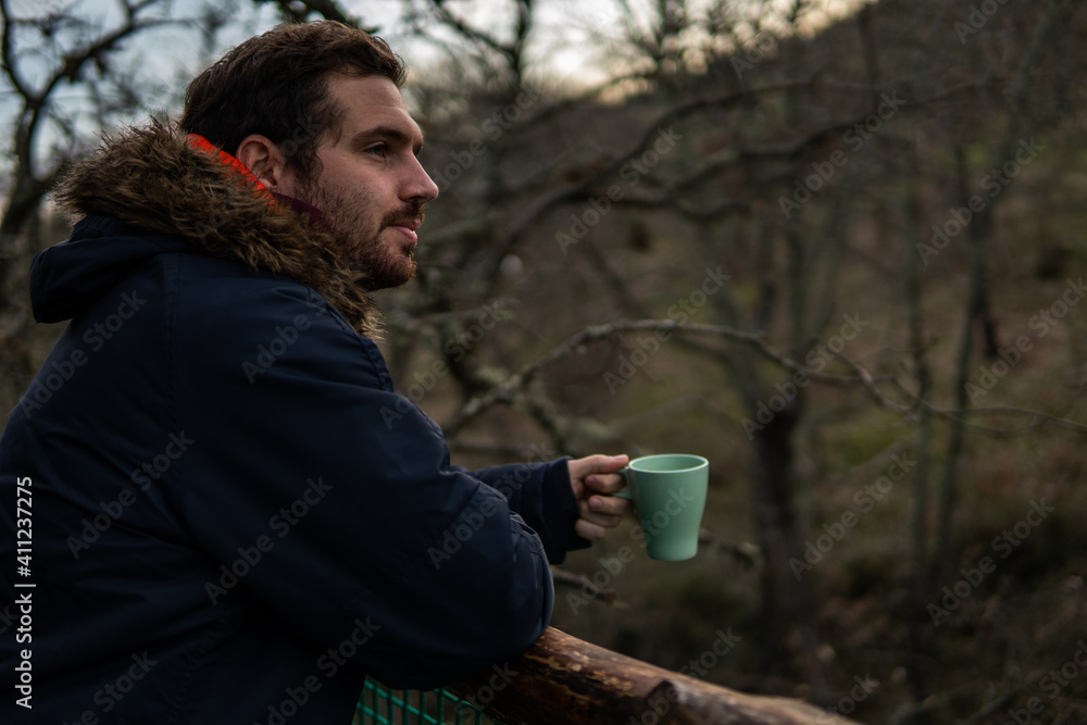 Photo of a young and attractive man having a coffee in the middle of a forest wearing winter clothes. Calm, empty place. Photo of a young and attractive man having a coffee in the middle of a forest wearing winter clothes. Calm, empty place.