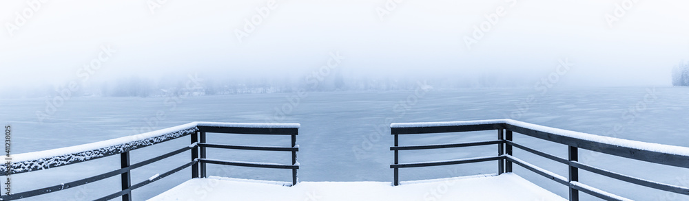 Mystical and silent snowy deck pier on frozen lake covered in snow in Finland during winter