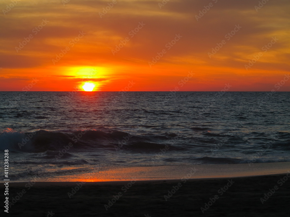 A beautiful red and orange sunset over the Pacific Ocean the silhouettes of beachgoers outlined against the water of Puerto Escondito, Mexico.  Image has copy space.