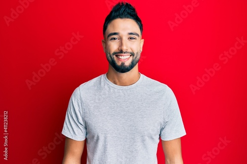Young man with beard wearing casual white tshirt with a happy and cool smile on face. lucky person.
